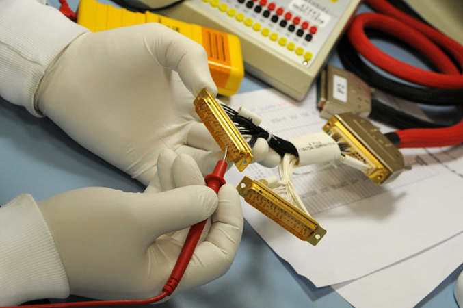 Mains gantées manipulant un composant électronique dans un atelier de Thales Alenia Space